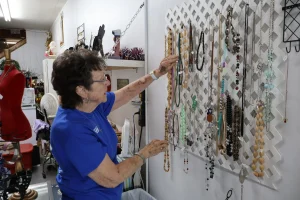 Senior volunteer in blue shirt arranging necklaces on a jewelry display wall at the Habitat ReStore Sebring